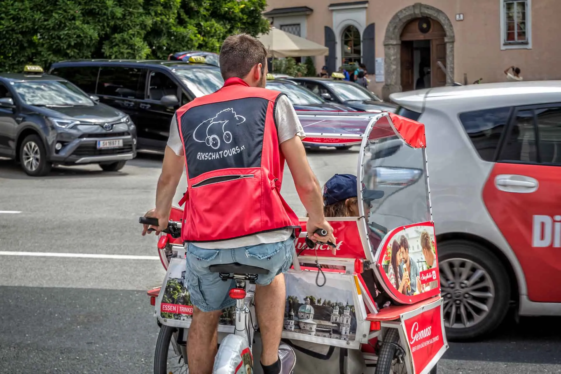 A rickshaw driver in a red vest riding through the city