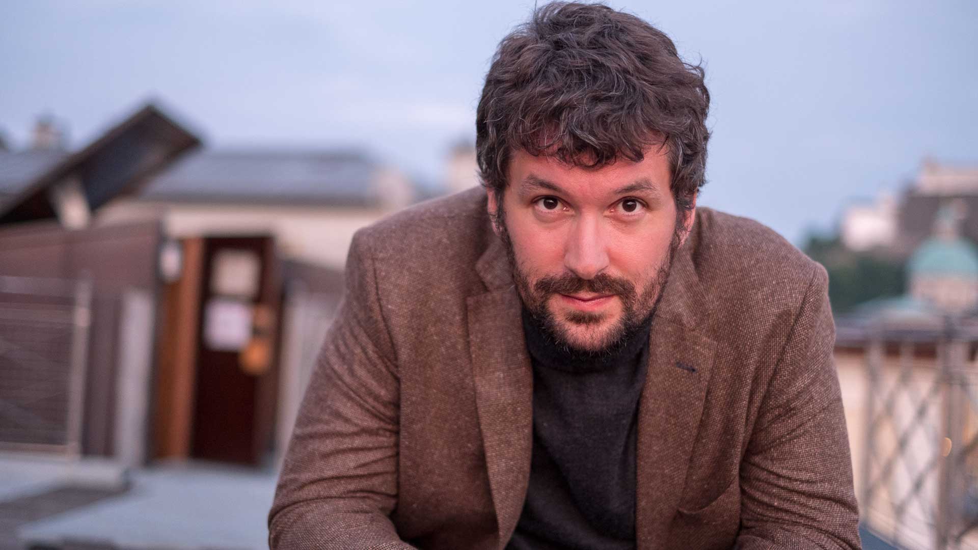 A man with a beard sitting on a rooftop.