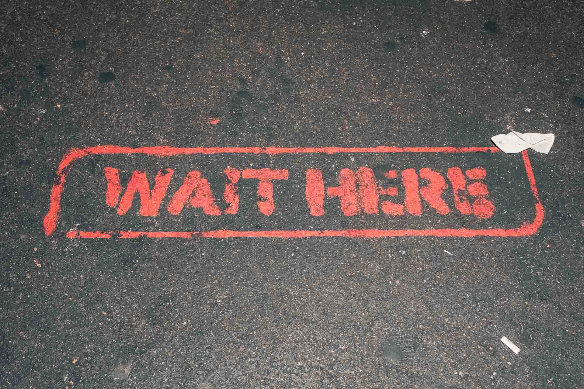 A sign that says wait here on the ground.