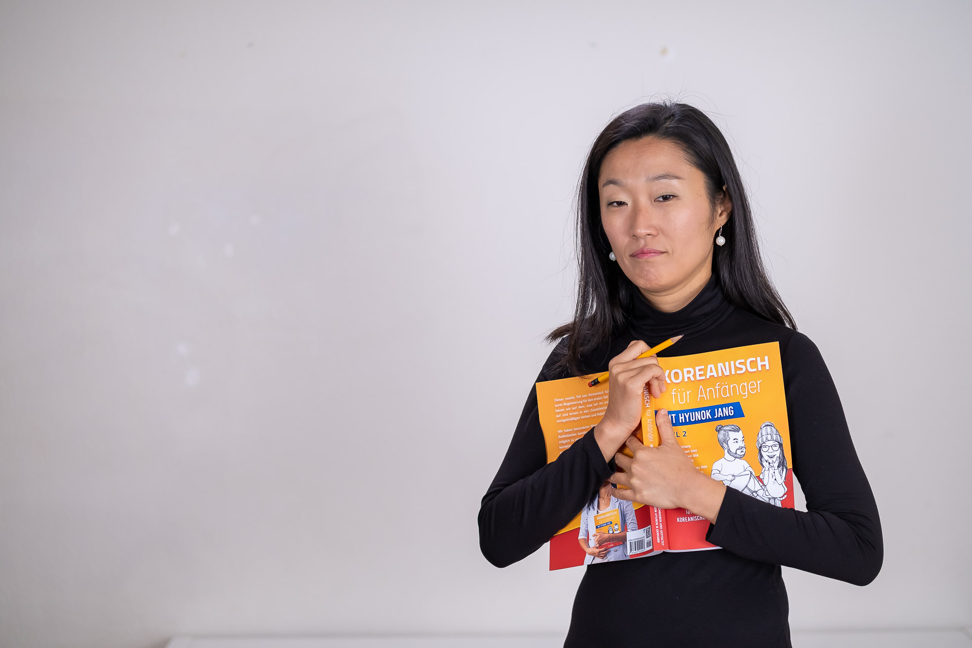 An asian woman holding a book in front of a white background.