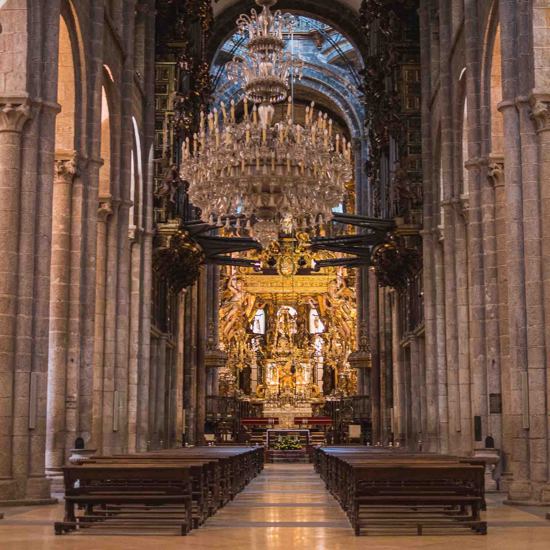 The inside of a cathedral with benches and chandeliers.